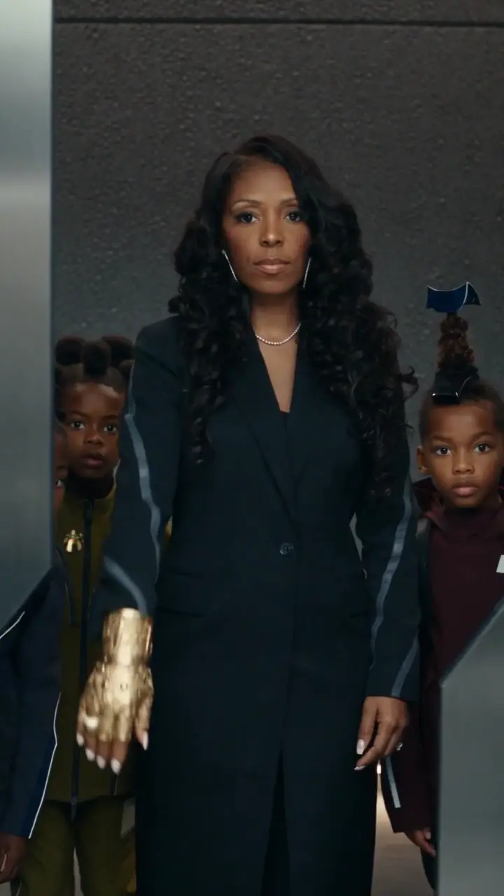 Ri Michelle in a tailored dark suit standing with two children in a cinematic corridor